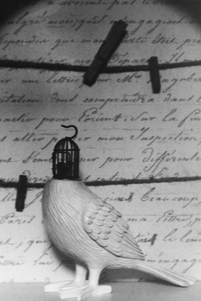 Bird figurine with a cage instead of a head against a background of cursive handwriting