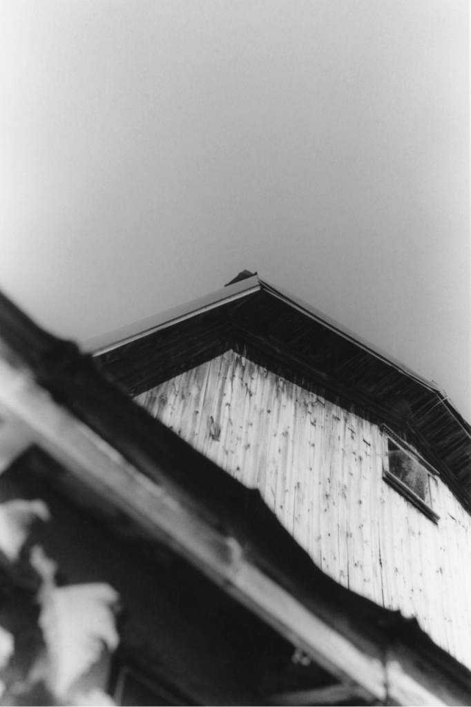Low-angle black and white view of a weathered wooden building against a pale sky.