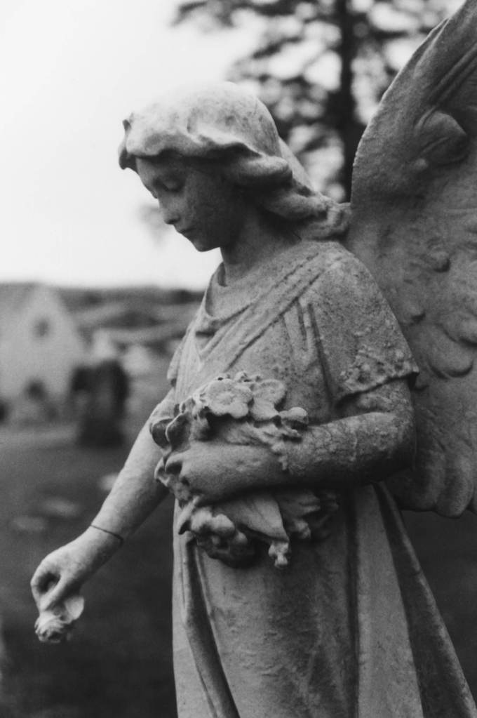 Stone angel statue looking down, holding a bouquet and a single flower