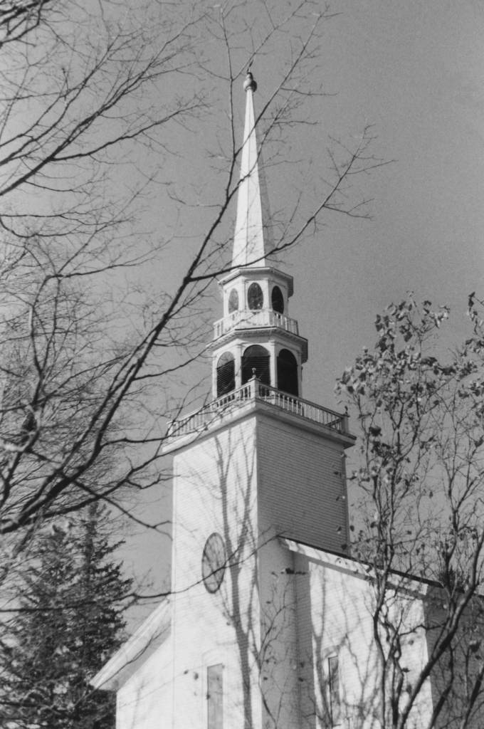 A white church steeple framed by bare tree branches in a black and white photograph.